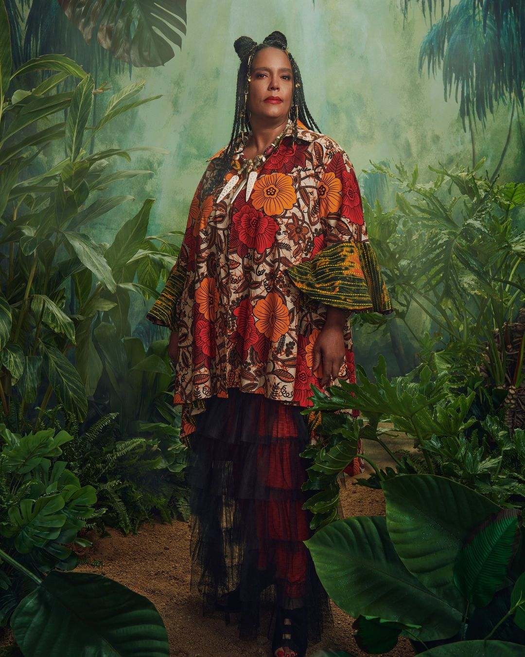 Adult female in a floral print dress poses in a lush jungle setting with a background of dense greenery and tropical foliage.